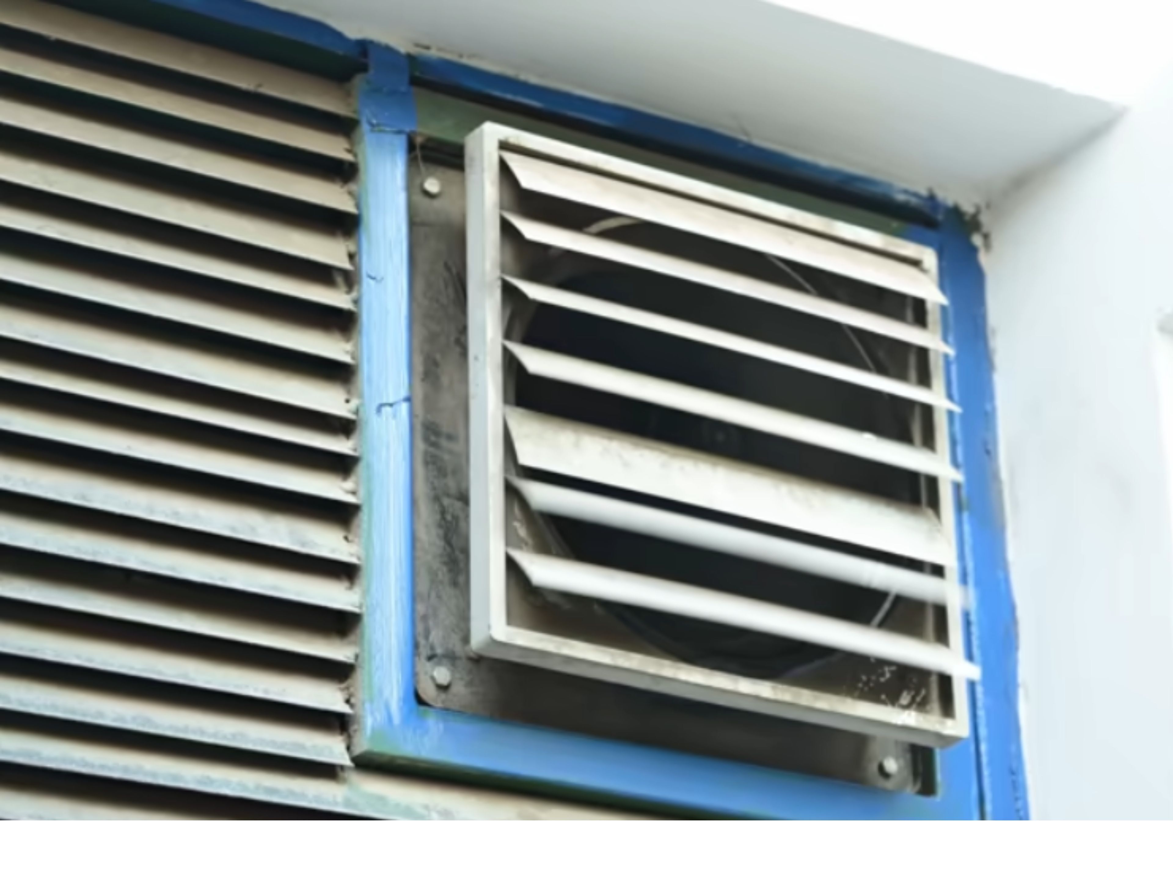 Exterior wall vent showcasing HVAC technology with metal louvers and ventilation fan.