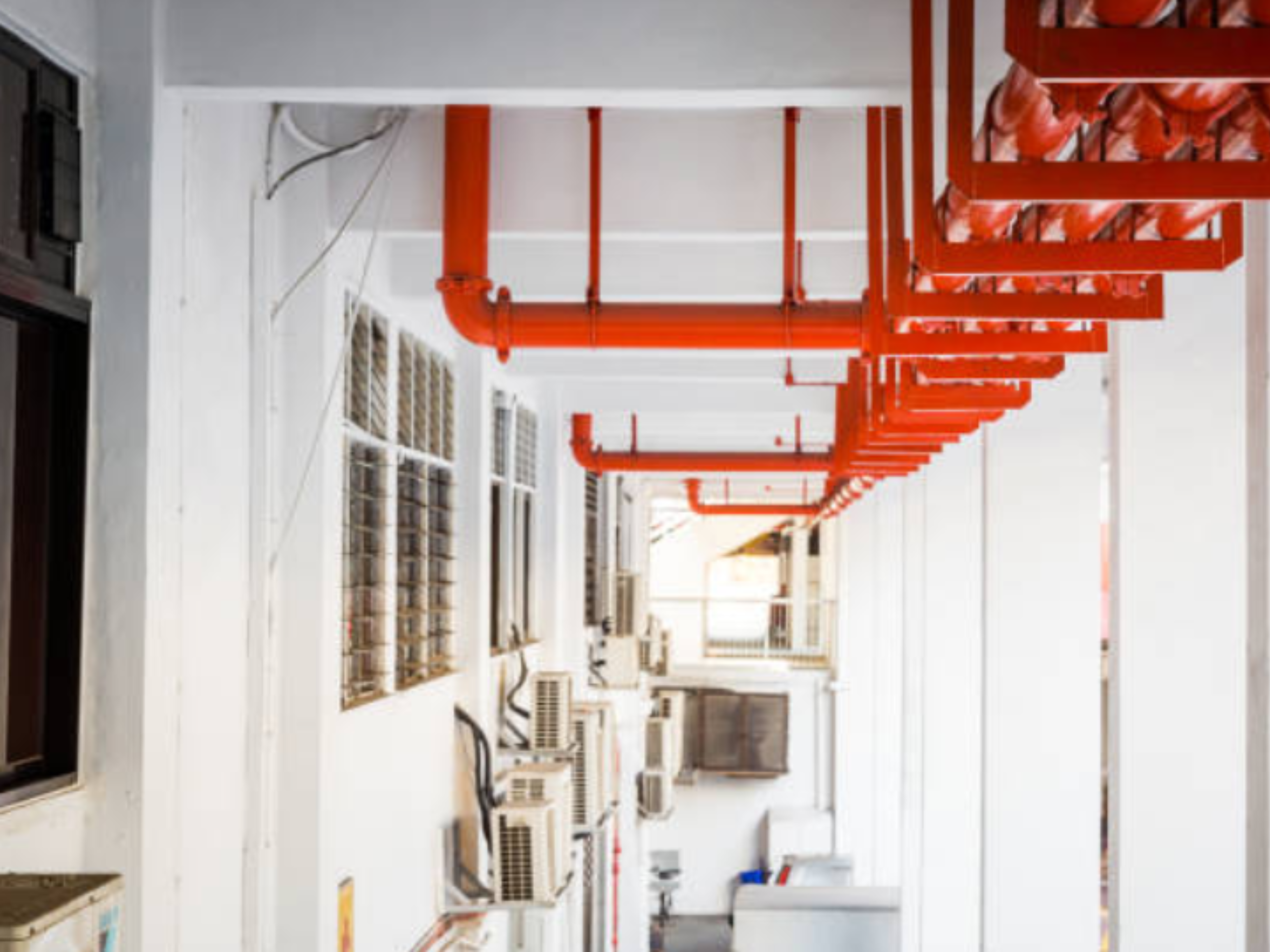Ceiling-mounted red fire damper and piping as part of commercial HVAC technology in a mechanical corridor.