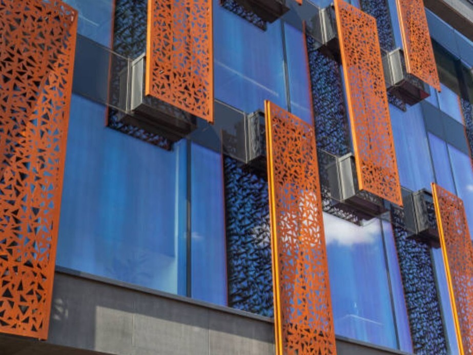 Orange perforated architectural screens mounted on a glass building façade for shade and design.
